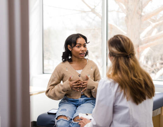 The young adult female patient gestures while explaining her mental health struggles with the doctor so she can receive some guidance.